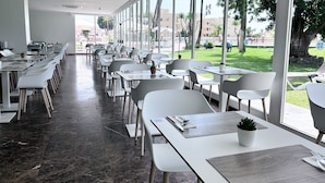 A modern dining area with white tables and chairs, large windows, and a view of the outdoors. - BLUESEA Al Andalus (Torremolinos)