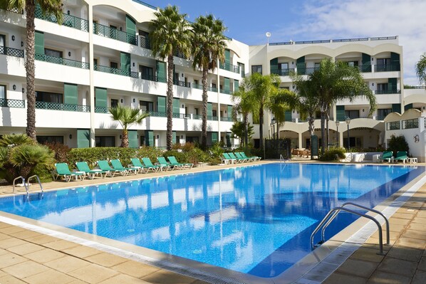 Una piscina al aire libre, sombrillas, sillones reclinables de piscina