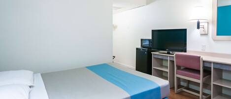 A hotel room with a bed, a desk with a computer, a chair, and a TV.