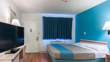 A hotel room with a bed, a TV, a desk, and a window with curtains.