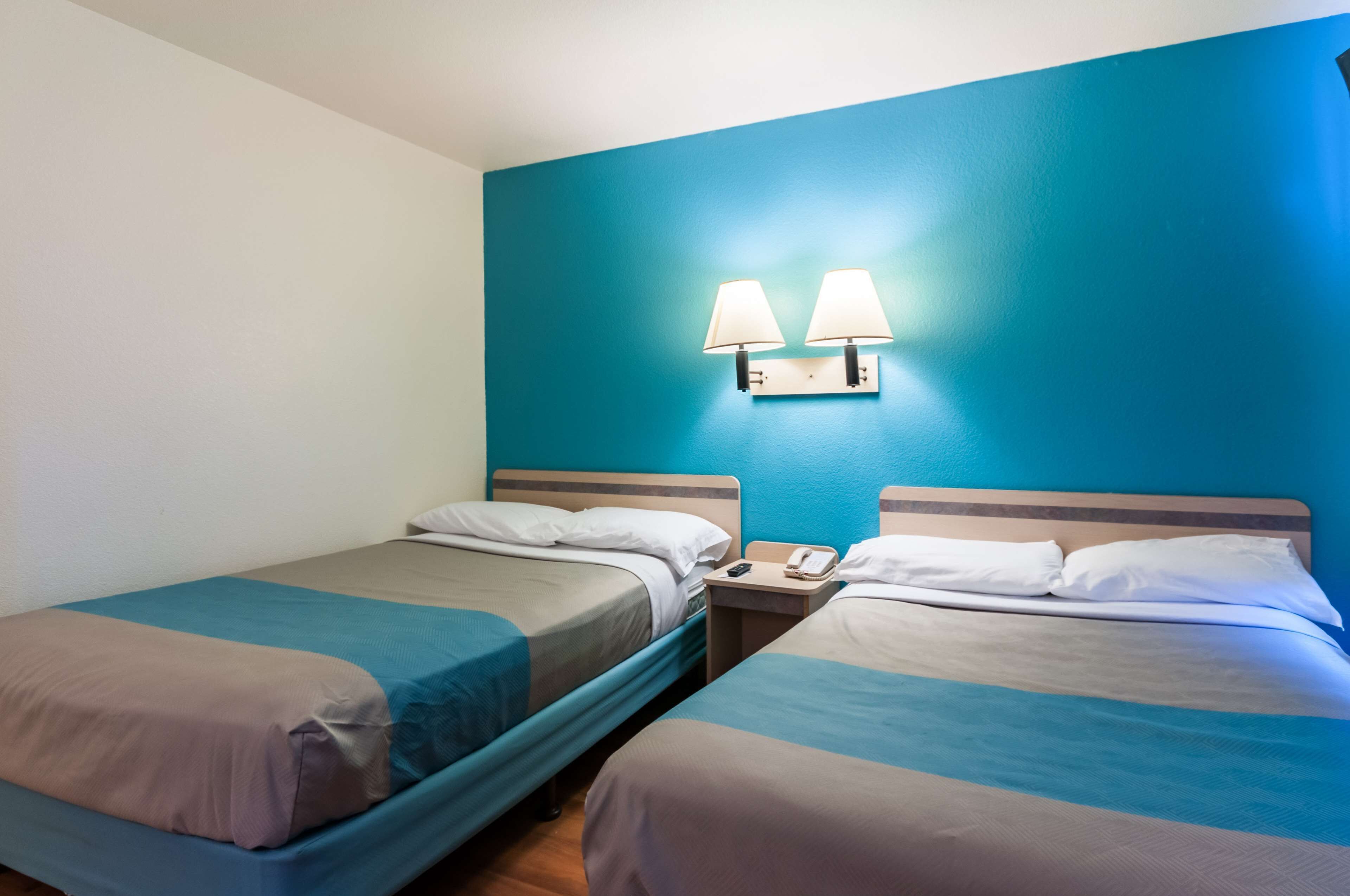 A hotel room with two single beds, a nightstand with a phone, and wall-mounted lamps.
