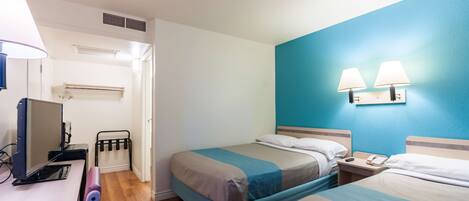 Een hotelkamer met twee bedden, een bureau met een computer, een bureaulamp en een wandradiator.