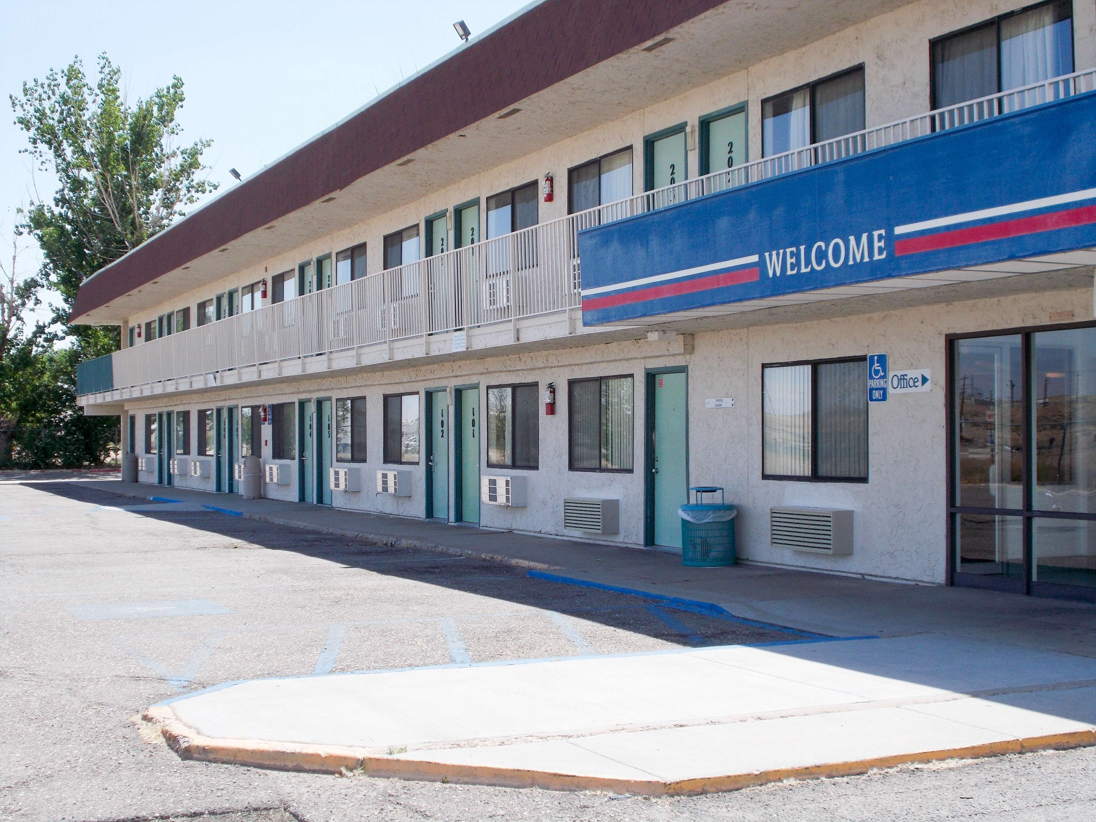 Un motel avec une enseigne « BIENVENUE », plusieurs chambres et un panneau indiquant les places de stationnement réservées aux personnes handicapées.
