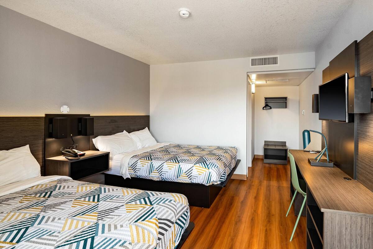 A modern hotel room with two beds, a desk, a TV, and a bathroom.