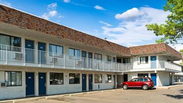 A motel with a brick facade, multiple balconies, and a red car parked in the driveway.