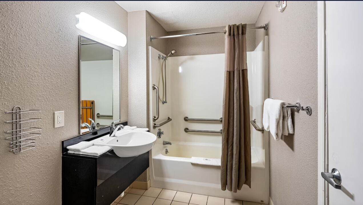 Un baño con lavamanos, espejo, ducha y toallero.