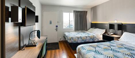 A hotel room with two beds, a desk with a chair, a TV, and a window with curtains.