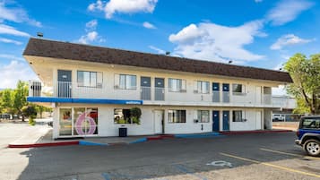 A two-story motel with a 'Welcome' sign, numbered rooms, and a parking lot.