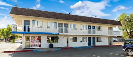Un motel de dos pisos con un letrero de 'Welcome', habitaciones numeradas y un estacionamiento.
