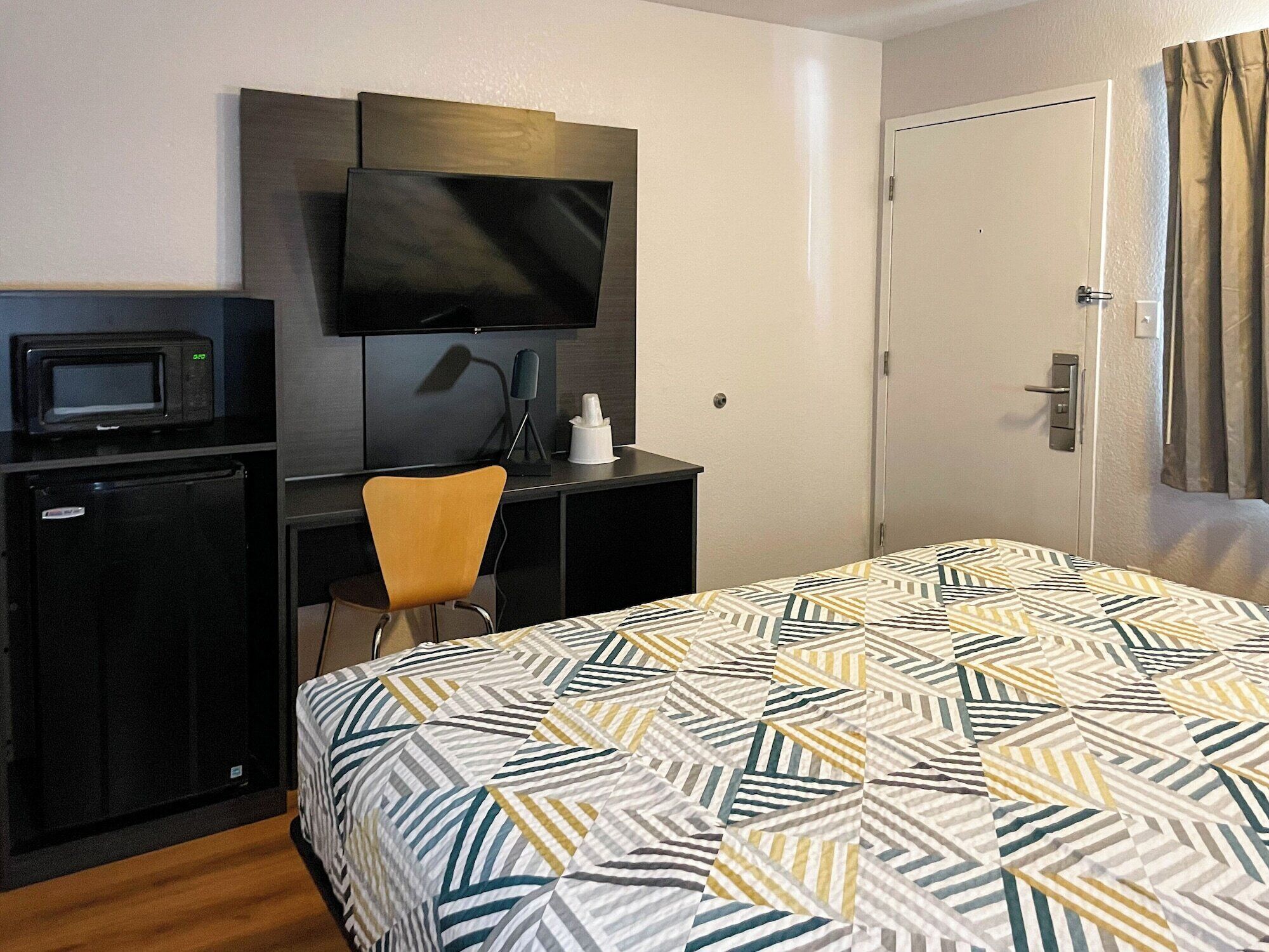A hotel room with a bed, a desk with a television, a microwave, and a small refrigerator.