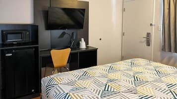A hotel room with a bed, a desk with a television, a microwave, and a small refrigerator.