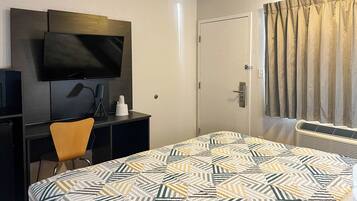 Une chambre d’hôtel avec un lit, un bureau avec une télévision, une chaise et une porte avec des rideaux.