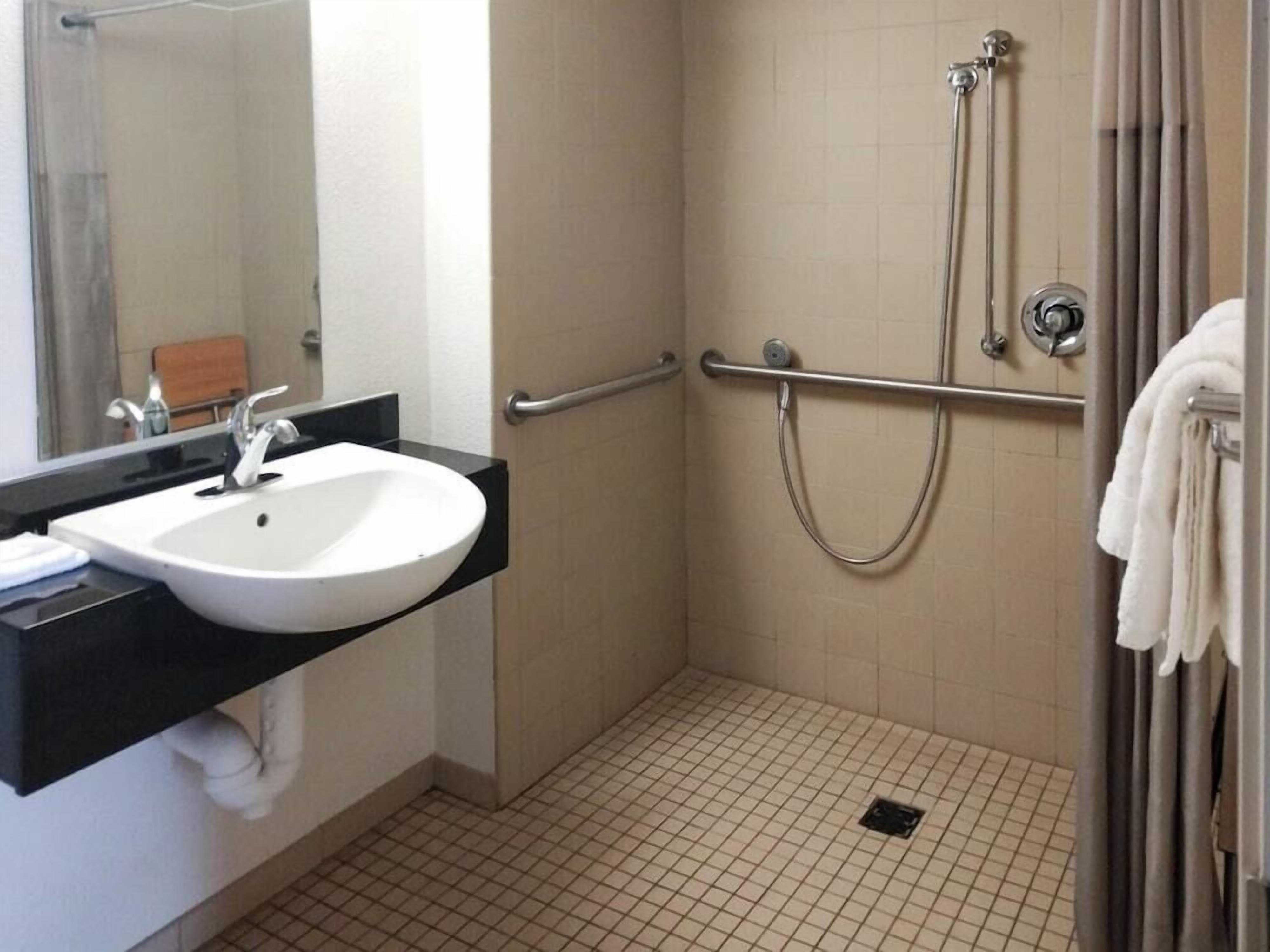A bathroom with a white sink, a mirror, a shower with a grab bar, and a towel rack.