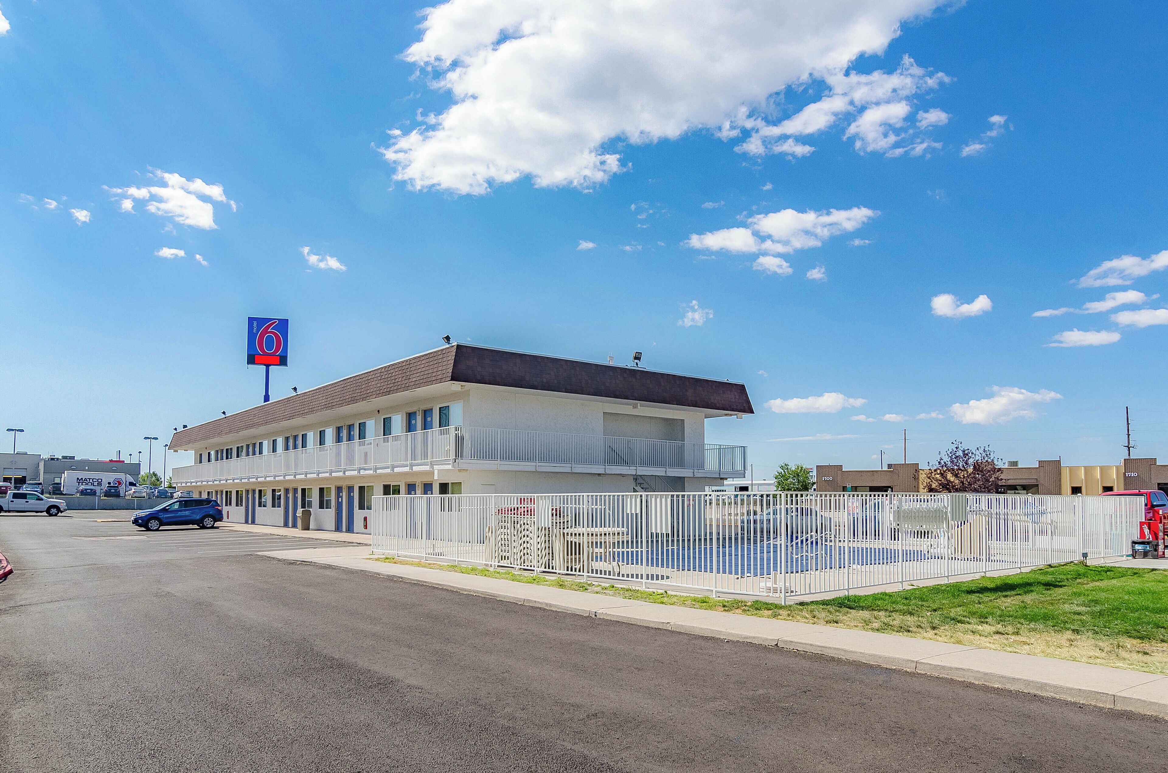 A motel with a two-story structure, a fenced parking area, and a clear blue sky.