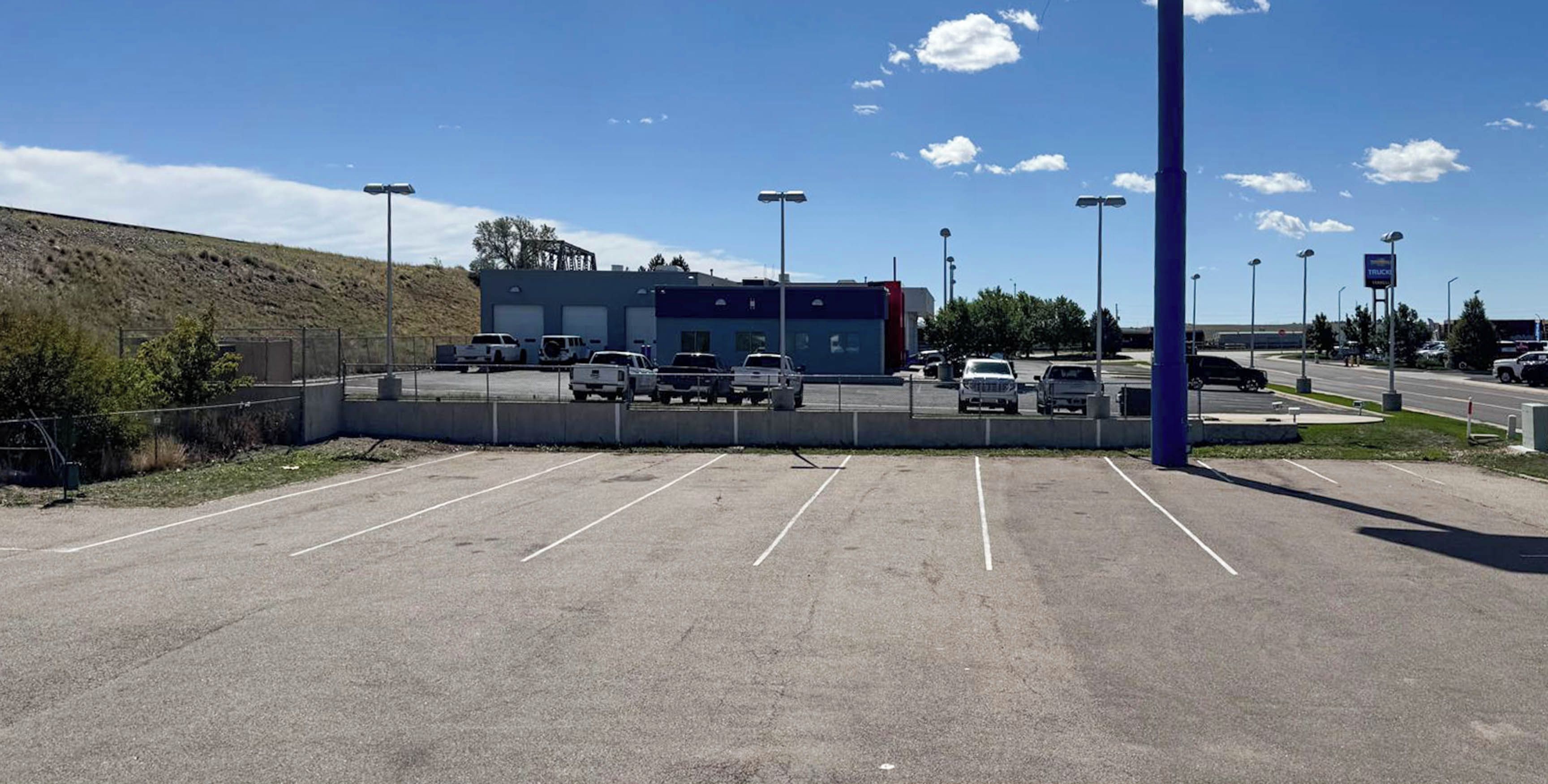 Un parking rempli de véhicules, un bâtiment à la façade bleue et un ciel dégagé.