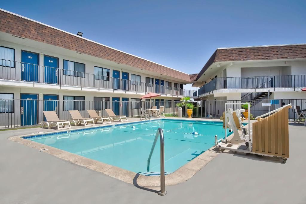 Un hôtel doté d’une piscine, de chaises longues et d’un bâtiment à deux étages avec des balcons.