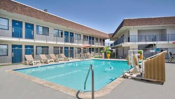 Un hôtel doté d’une piscine, de chaises longues et d’un bâtiment à deux étages avec des balcons.