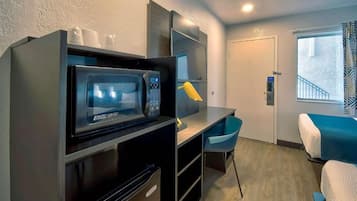 A compact room with a kitchenette, a bed, a desk, and a chair.