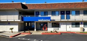 A building with a 'welcome' sign, a number '6' sign, and a parking lot. - Motel 6 Palmdale, CA (Palmdale)