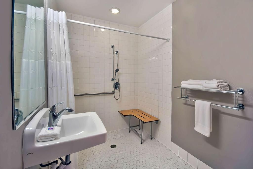 Een badkamer met een witte wastafel, een douche, een houten kruk en een handdoekhouder.