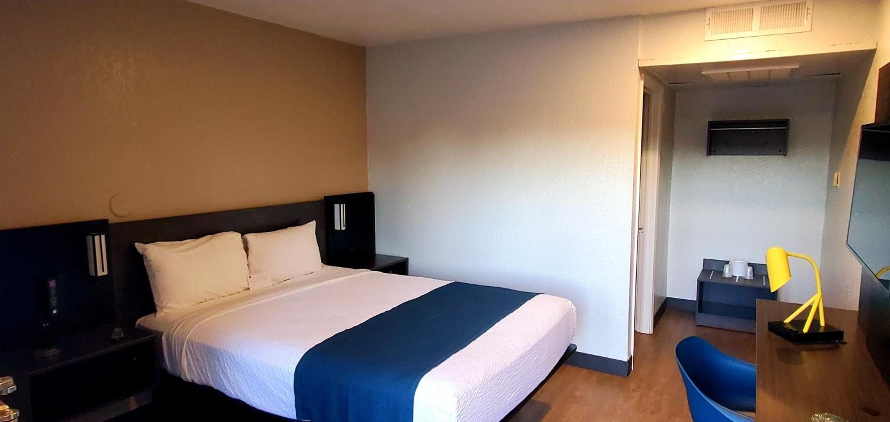 Habitación de hotel con cama, escritorio, silla, televisor y puerta que da a otra habitación.