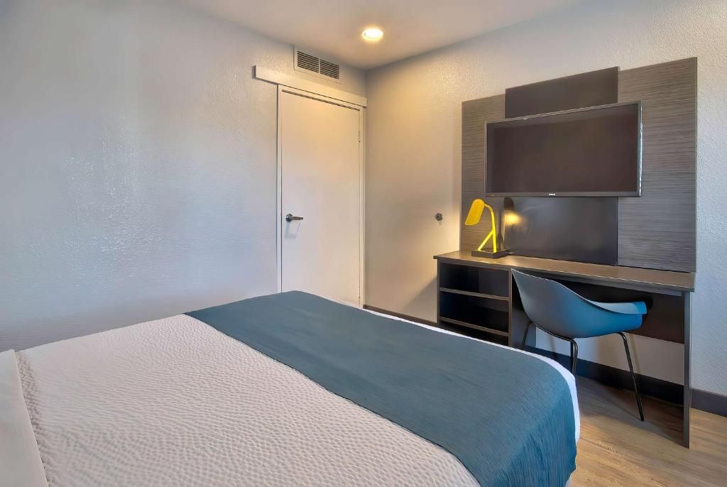 A hotel room with a bed, a desk, a chair, a television, and a door.