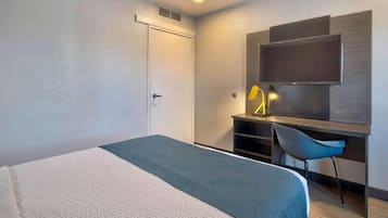 A hotel room with a bed, a desk, a chair, a television, and a door.