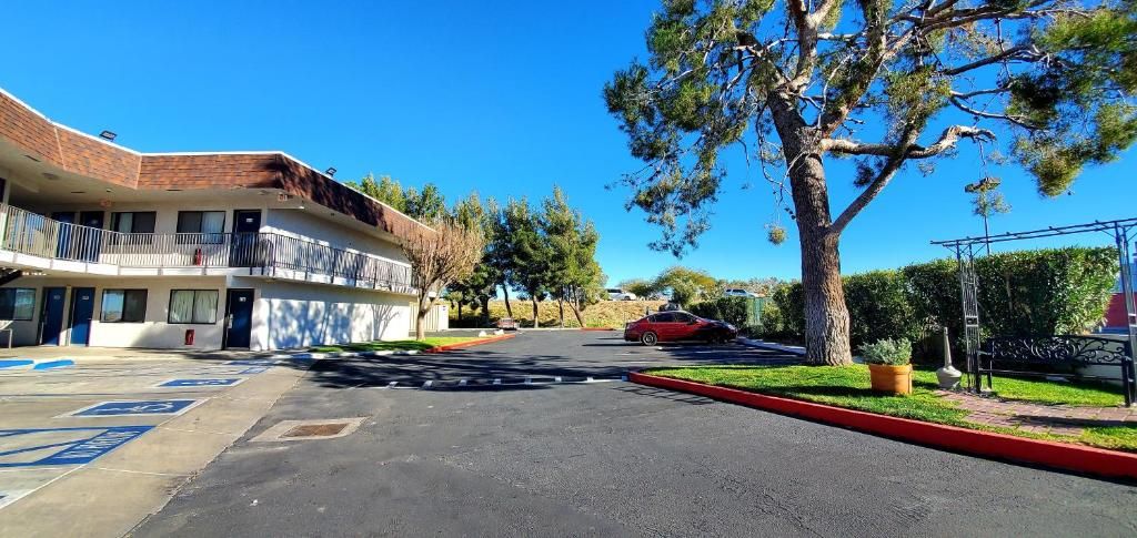 A multi-story motel with a parking lot, a red car parked in front, and a large tree to the right.