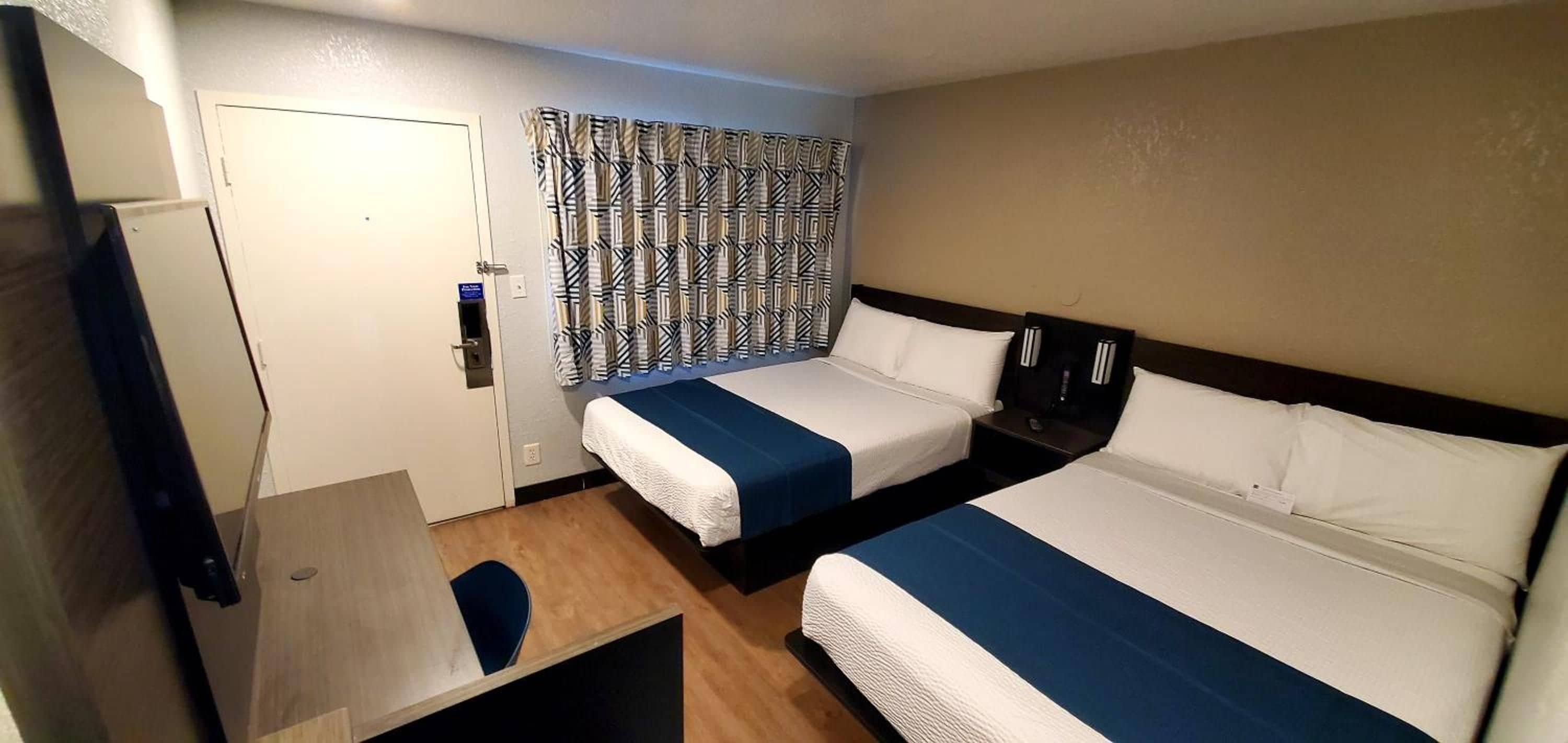 Une chambre d’hôtel avec deux lits, un bureau, une chaise, une armoire et un rideau à motifs.