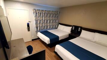 Une chambre d’hôtel avec deux lits, un bureau, une chaise, une armoire et un rideau à motifs.