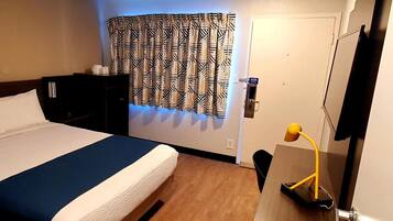 Habitación de hotel con cama, mesita de noche, lámpara y ventana con cortinas estampadas.