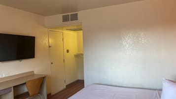 A hotel room with a bed, a desk with a chair, a TV mounted on the wall, and a door leading to a bathroom.
