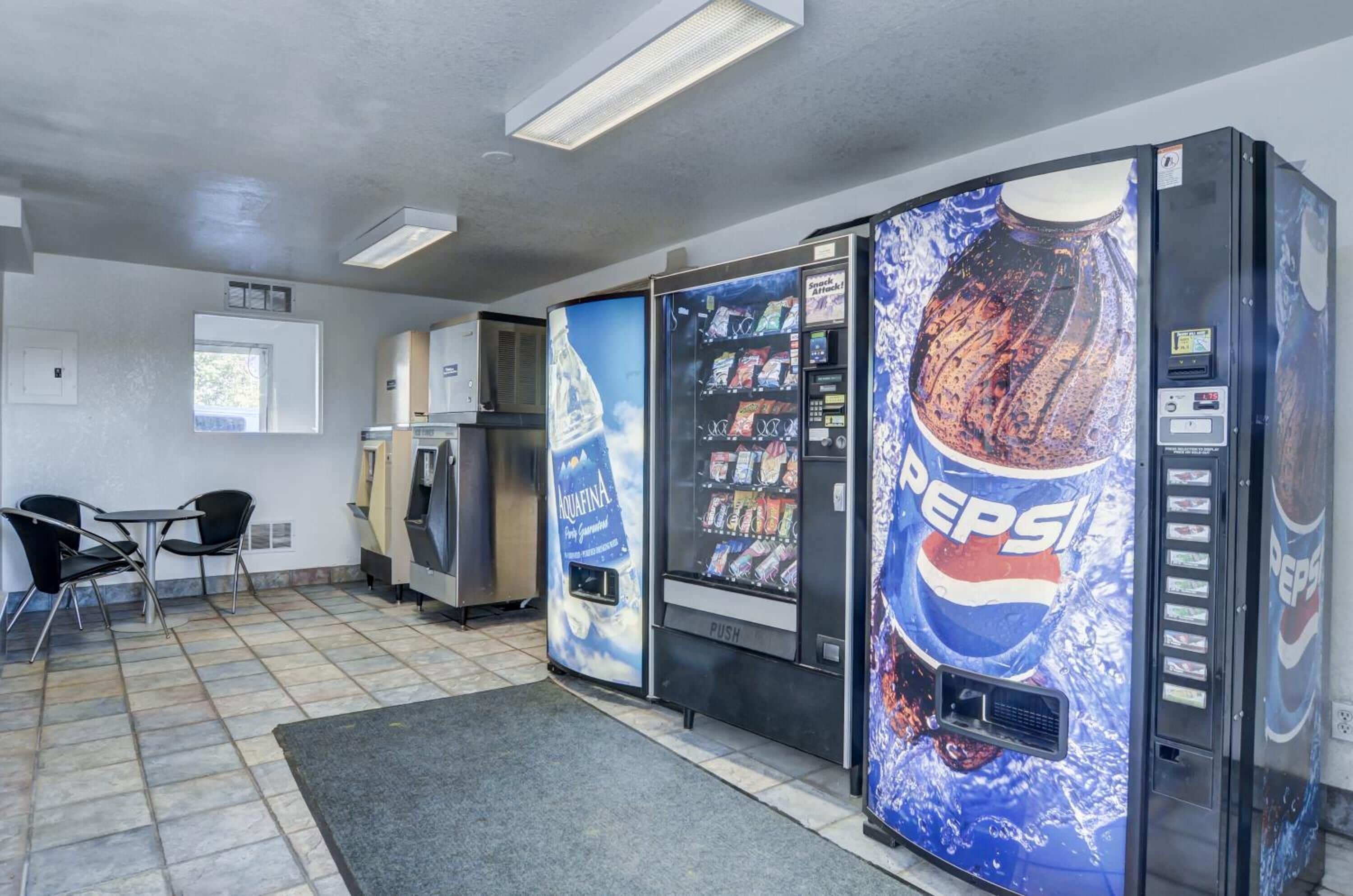 A room with a kitchenette, a refrigerator, a microwave, a water dispenser, and a seating area with chairs.