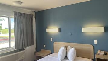 Ein Hotelzimmer mit einem Bett, einem Nachttisch, einem Telefon und einem Fenster mit Vorhängen.