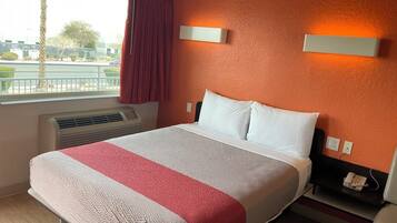 A hotel room with a large bed, a window with a view of the outside, a wall-mounted phone, and a heater.
