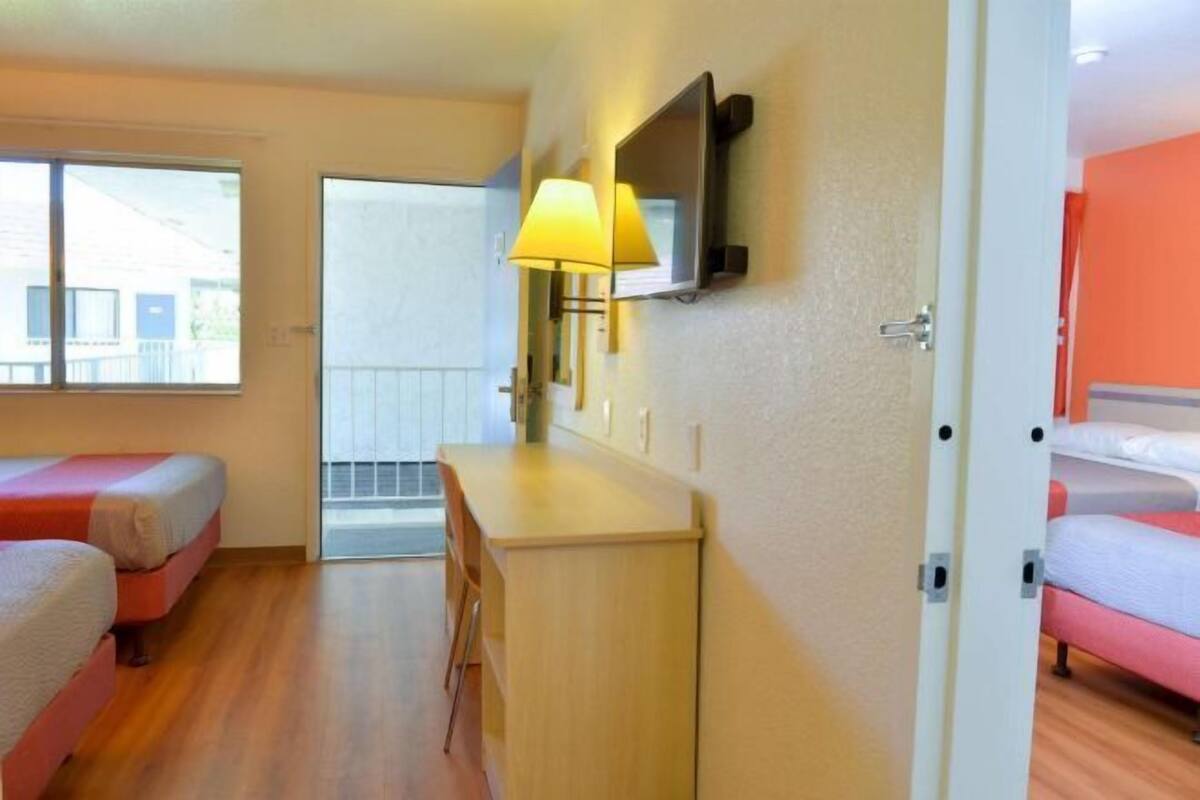 A hotel room with two single beds, a desk, a chair, a TV mounted on the wall, and a window providing a view of the outside.