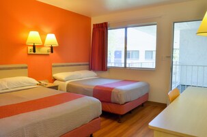 Habitación de hotel con dos camas, ventana con vistas, una mesa y una lámpara.