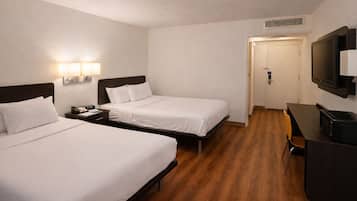 A hotel room with two beds, a desk, a chair, a TV, and a door leading to a bathroom.