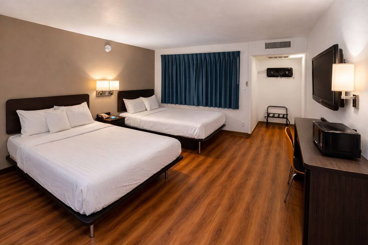 A hotel room with two beds, a desk with a chair, a TV, and a window with curtains.
