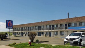 A motel with a '6 ENTER' sign, a parking lot, and a white car parked in front. - Motel 6 Ontario, OR (Ontario)