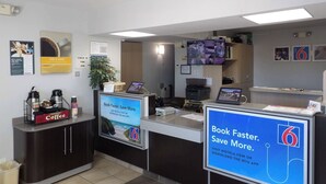 Un mostrador de recepción con una estación de café, una pantalla de televisión y un cartel que promociona una aplicación para reservas.