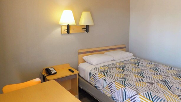 Una habitación de hotel con una cama, un escritorio y dos lámparas fijadas a la pared.