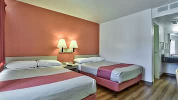 A hotel room with two beds, a nightstand, and a bathroom visible through an open door.