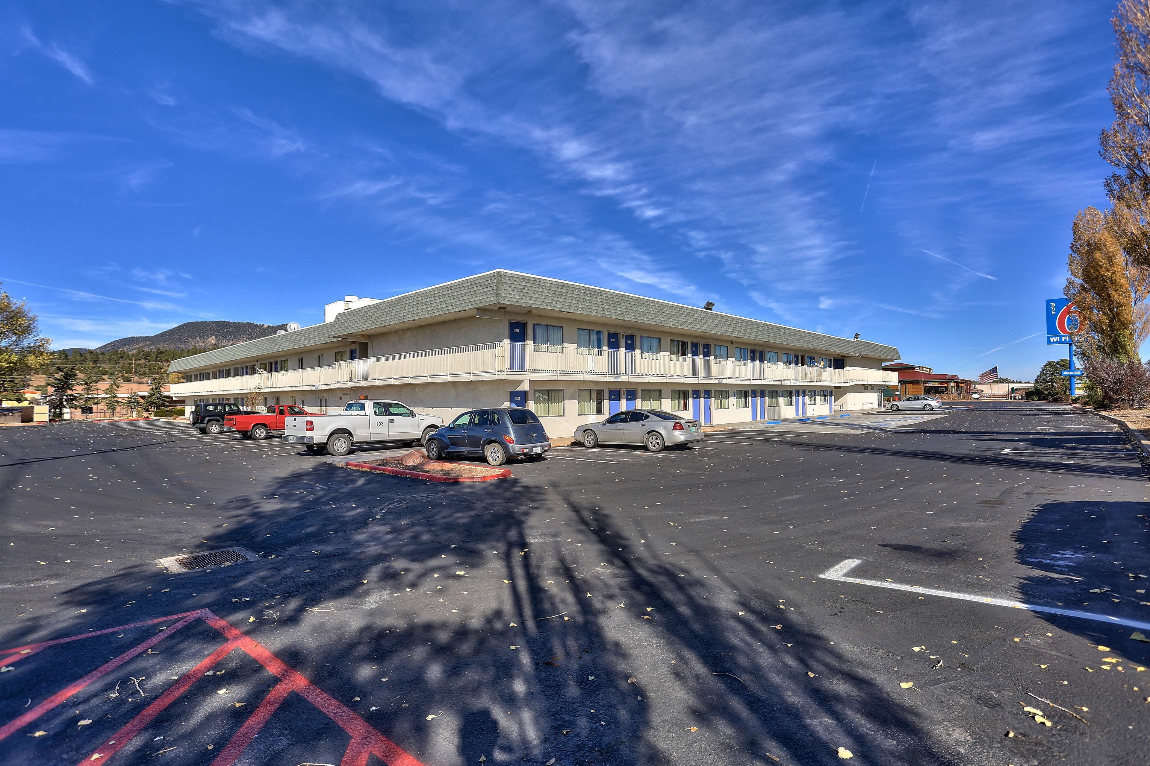 A parking lot with several cars, a building with a flat roof, and a clear blue sky.