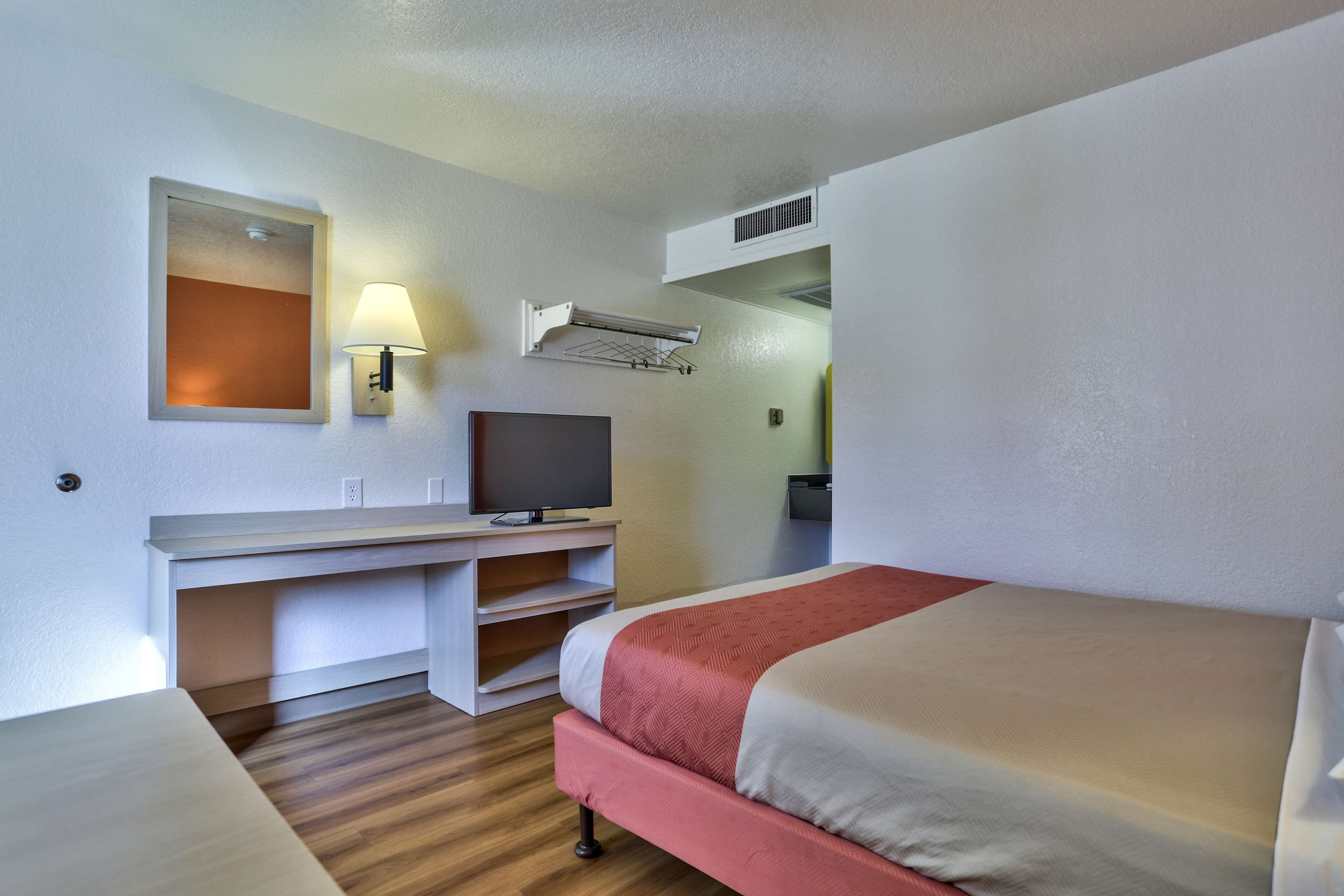 Een hotelkamer met een bed, een bureau met een televisie, een wandlamp en een airconditioner.