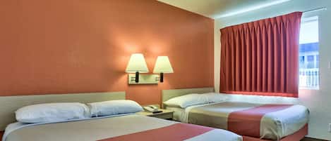 Une chambre d’hôtel avec deux lits, une table de chevet avec un téléphone et une fenêtre avec des rideaux rouges.