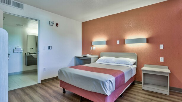 A hotel room with a bed, bedside tables, a mirror, and a bathroom visible through an open door. - Motel 6 Flagstaff, AZ - Butler (Flagstaff)