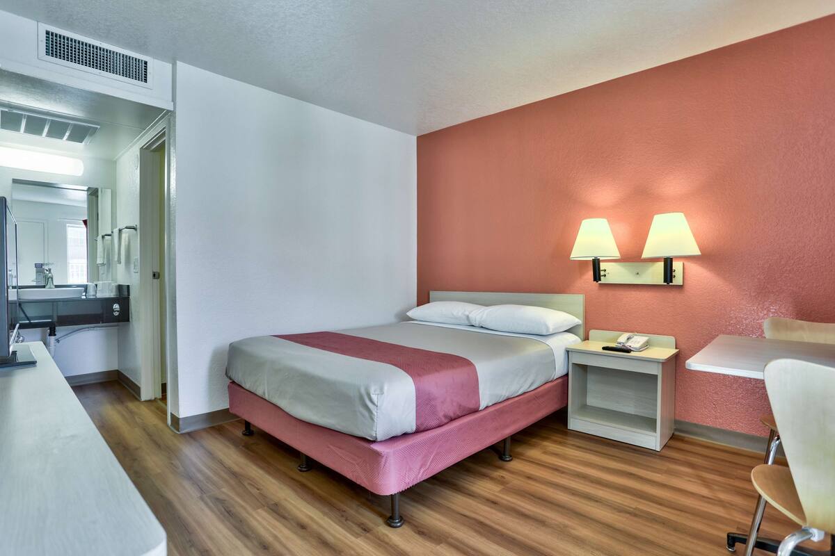 A hotel room with a bed, bedside table, lamp, desk, chair, and a mirror.