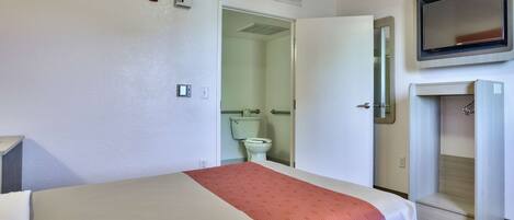 Ein Hotelzimmer mit Bett, Badezimmer mit Toilette und Waschbecken sowie einem an der Wand montierten Fernseher.