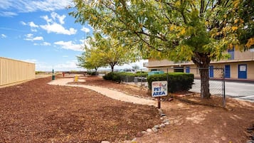 A motel with a pet area sign, a fenced parking lot, and a building with a blue awning.